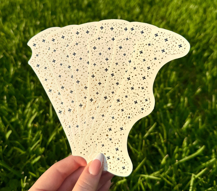 Hand holding a sheet of adhesive face sparkle gems over grass