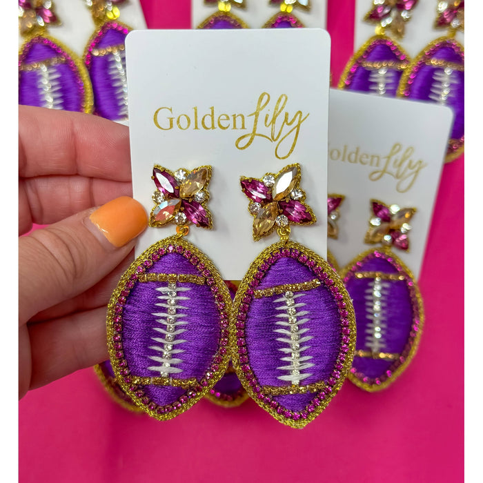 Hand holding purple and gold beaded football earrings on Golden Lily cards