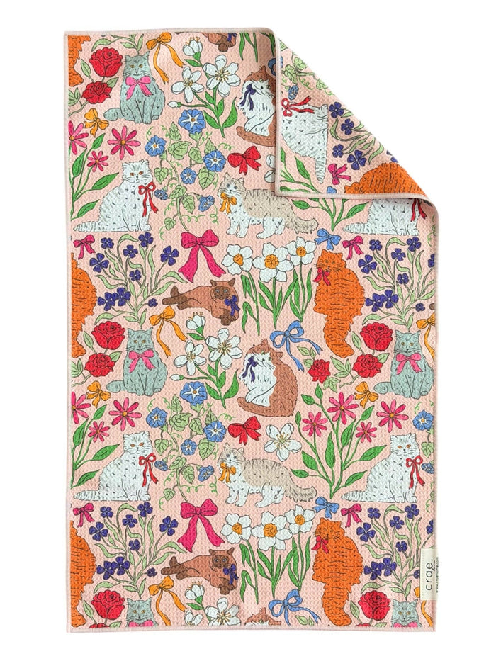 Pink fabric with a repeating pattern of cats wearing bows surrounded by flowers and ribbons