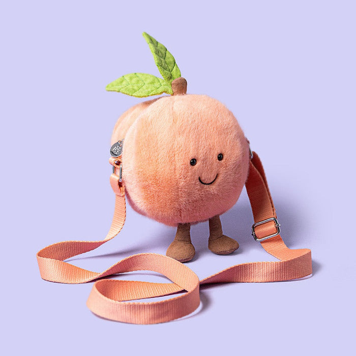 Plush peach shaped crossbody bag with a smiling face and small brown legs on a light purple background
