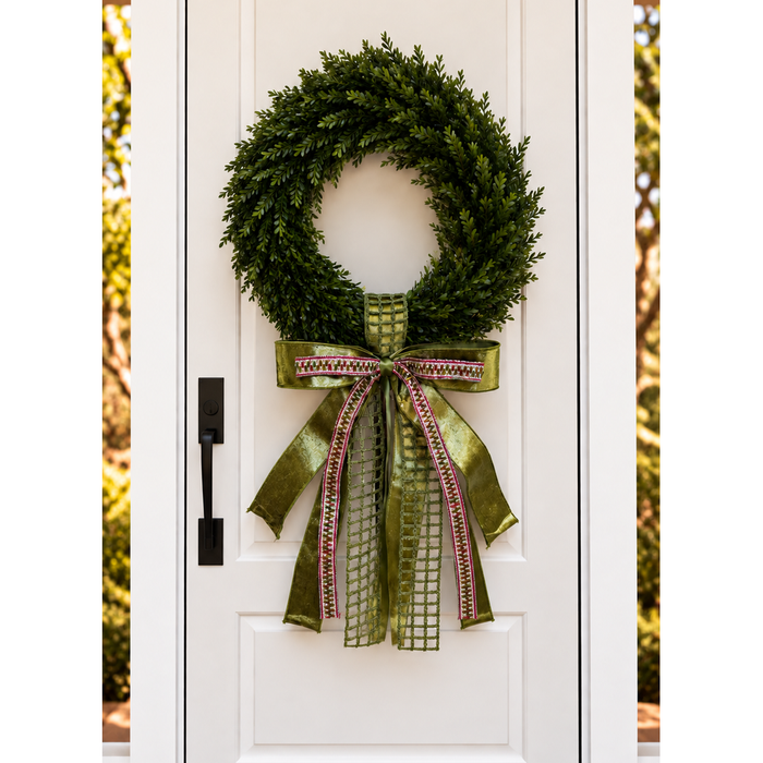 White front door with a boxwood wreath and an olive green ribbon bow with pink woven trim