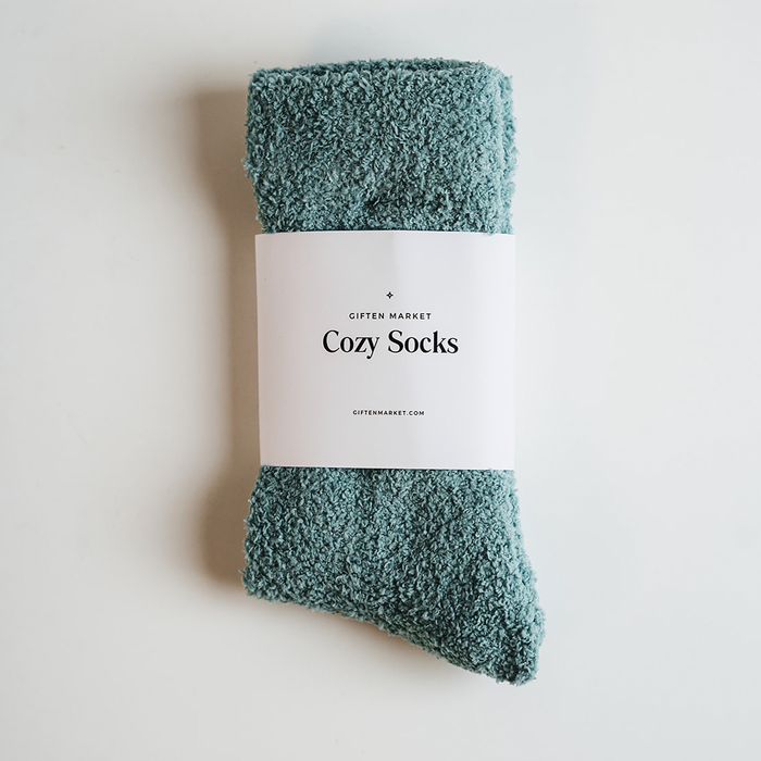 Teal fuzzy socks with a white paper band labeled Giften Market Cozy Socks