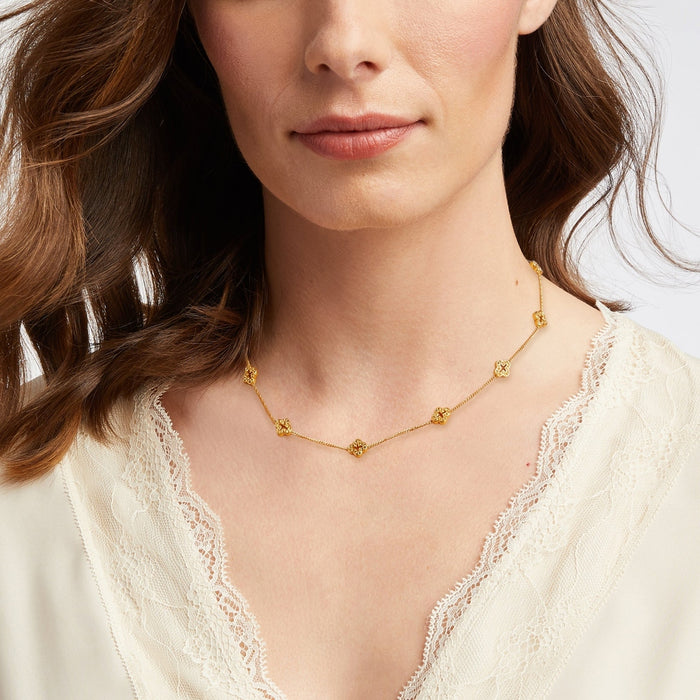 Gold chain necklace with small clover shaped charms worn by a woman