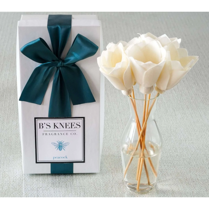 White gift box with teal ribbon and B's Knees Fragrance Co label next to a glass vase with white flower reed diffusers