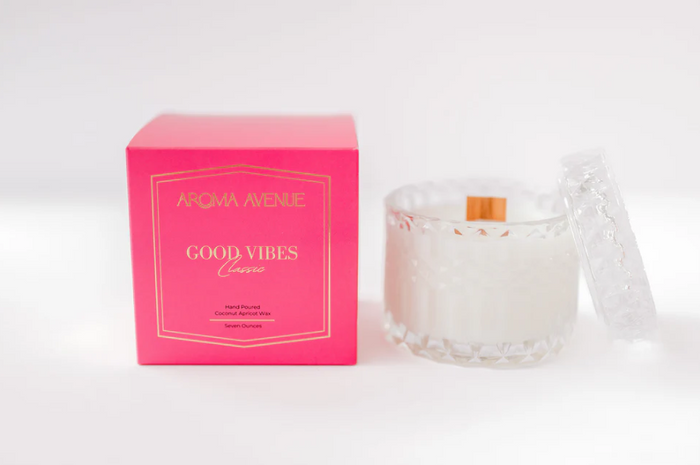 Good Vibes candle in a faceted glass beside its pink box