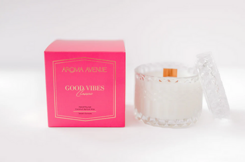 Good Vibes candle in a faceted glass beside its pink box