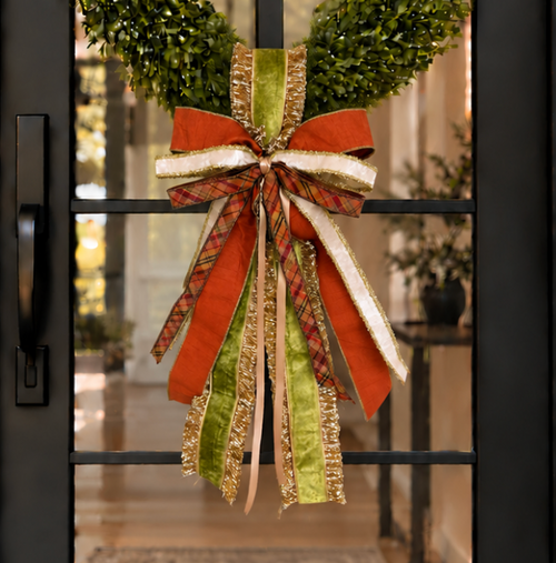 Door sash and bow in rust orange, cream, green and gold ribbon hanging from a boxwood wreath