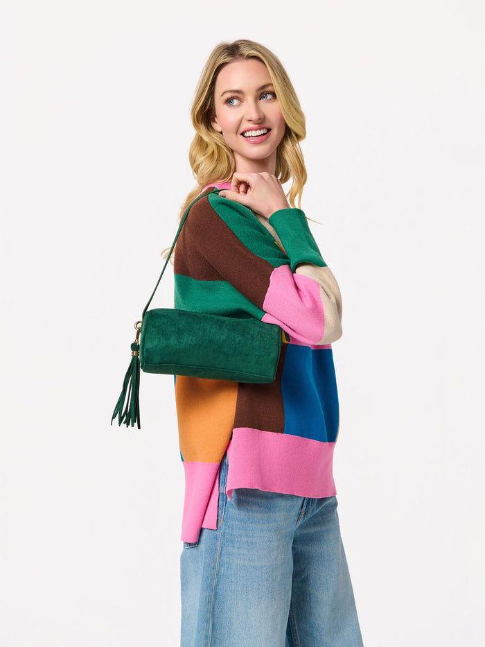 Woman wearing a color block sweater and jeans carrying a green suede cylindrical shoulder bag with a tassel