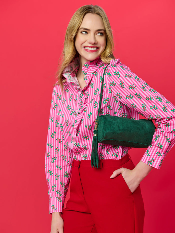 Woman wearing a pink striped shirt with green leaf pattern and red trousers carrying a green suede cylinder bag