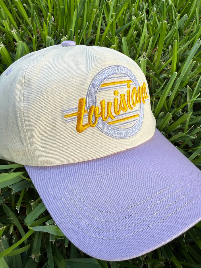 Cream and lavender baseball cap with Louisiana embroidery on green grass