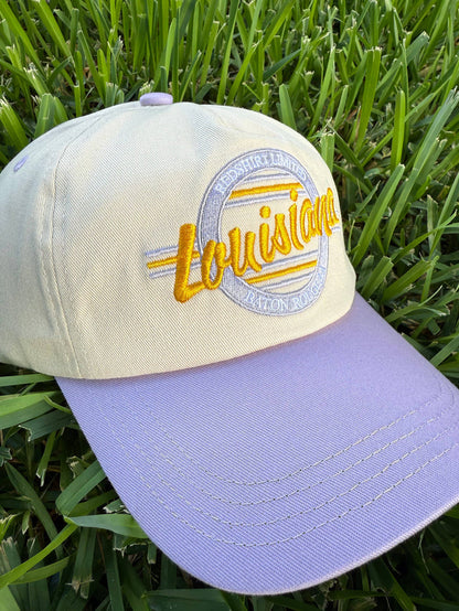 Cream and lavender baseball cap with Louisiana embroidery on green grass