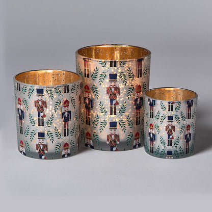 Three glass candle holders with nutcracker and leaf patterns