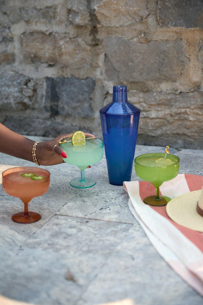Colorful acrylic cocktail shakers and drinks on an outdoor stone table
