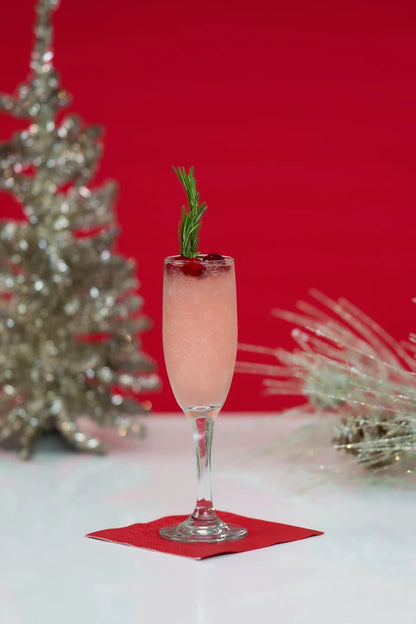 Pink cocktail in a champagne flute garnished with rosemary and cranberries on a red napkin