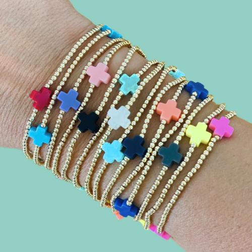 Stack of gold beaded bracelets with colorful cross charms on a wrist