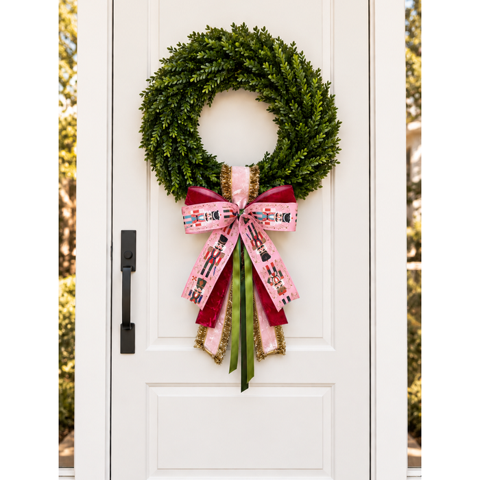 White front door with a boxwood wreath and a pink nutcracker-print ribbon bow