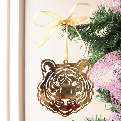 Gold tiger head ornament hanging from a Christmas tree branch with a gold ribbon bow